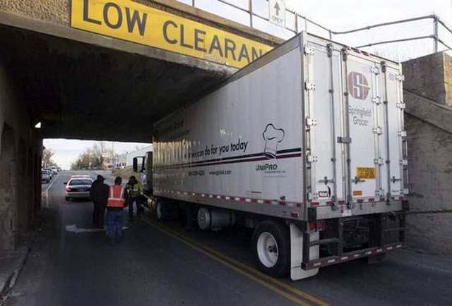 There is a truck stuck under a bridge and no one can