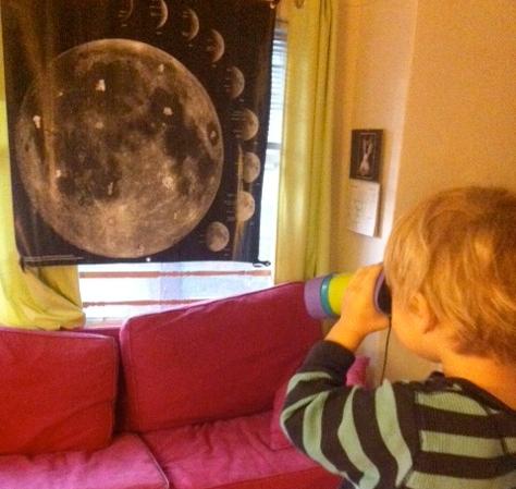 Hide & Seek Moon Children use binoculars to search for small items that an astronaut lost while walking on the Moon. The Moon is pictured on a banner hanging a short distance away.