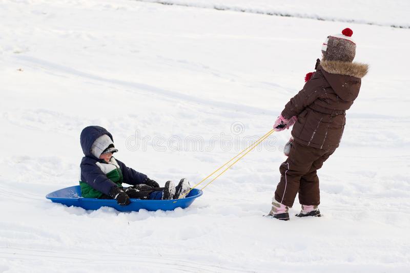 A kid pulls his lazy little brother in a sled