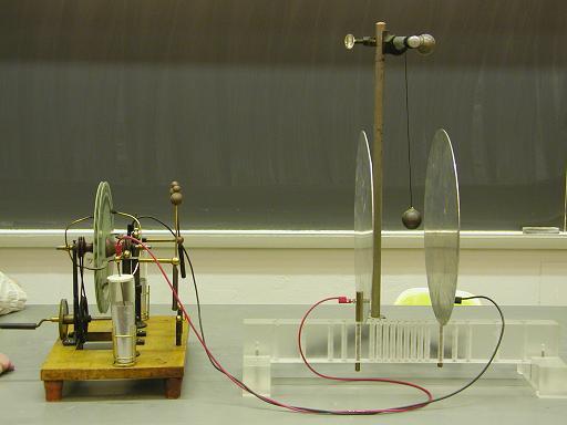 Electrostatic Ping Pong Description: A Wimshurst machine is connected to parallel aluminum plates. A ping pong ball coated with conducting paint is suspended between the plates.