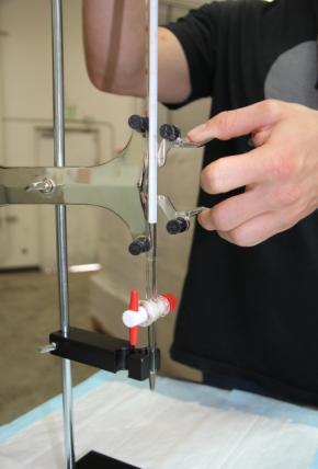 6. Carefully open the Double Burette Clamp's spring arms with your thumb and forefinger and place the burette in between the four indentations in the double burette clamp's spring arm's plastic knobs.