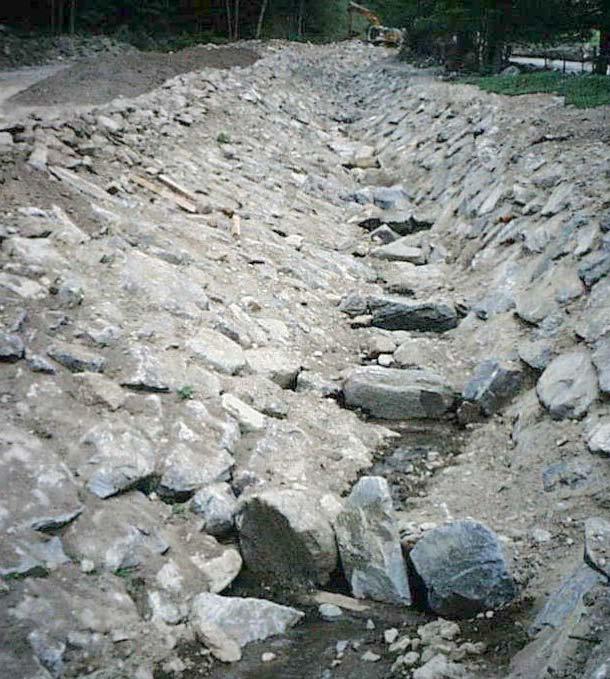 The channel has an open, natural bottom with varying width fixed by low sills made of boulders founded on timber logs.